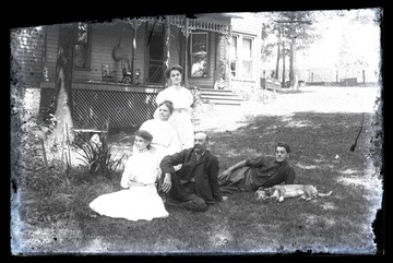 A man, his wife, their three children and family pet relax on the lawn outside of their home. 