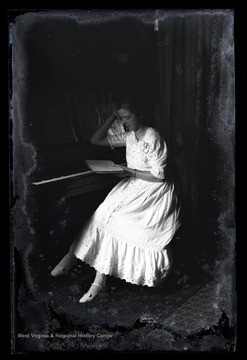 A young, unidentified girl leans against a piano as she reads a book. 