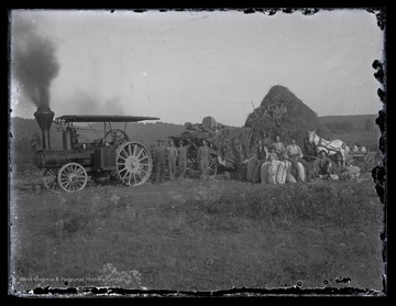 On the left is a Geiser Manufacturing Company steam tractor engine, also known as road locomotives, which likely pulled these farmers ploughs behind them. In the center is likely a threshing machine for the separation of grain from stalks and husks. On the right, a group of men sit with tightly bound bags, likely holding the grain seed. 