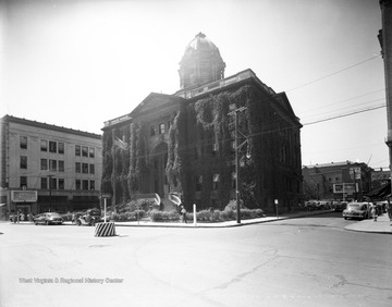 Street view of the ivy covered building. "The capitol annex sat at the corner of Lee and Hale Streets and housed the offices of the auditor, treasurer, the Supreme Court, the state law library, the adjutant general, and the Department of Archives and History until the new capitol was completed in 1932. The building later housed the Kanawha County Public Library from 1926 to 1966 and Morris Harvey College from 1935 to 1947. The building was demolished in 1967."
