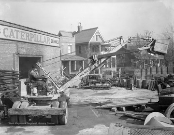 A man operates a Michigan loading shovel behind a building reading, "... Caterpillar Service."