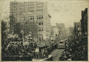 A crowd lines each side of High Street as parade floats travel down the street at 10 a.m.  The first float visible is shaped like a clothes iron.