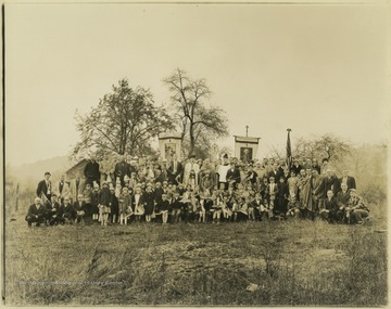 A group holding American flags gather together for a group photo in a field. Three men at the center of the image look to be priests or other members of the clergy.