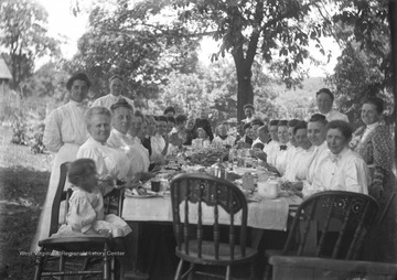 Members of the Green family pose at an outdoor dining table during a meal.  The covering on the table is sheets of newspaper.