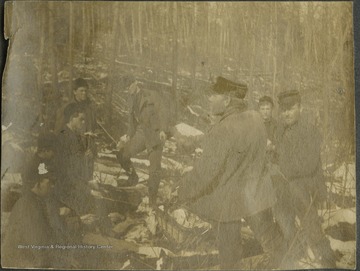 A group of Baltimore and Ohio surveyors huddle by a fire to toast bread in the snow covered woods.This photograph is found in a scrapbook documenting the survey for the B. & O. Railroad in West Virginia and surrounding states. 