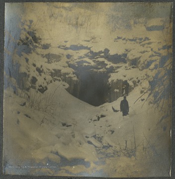 A man stands knee deep in snow just outside of the tunnel entrance while surveying for the Baltimore and Ohio Railroad Company.This photograph is found in a scrapbook documenting the survey for the B. & O. Railroad in West Virginia and surrounding states. 