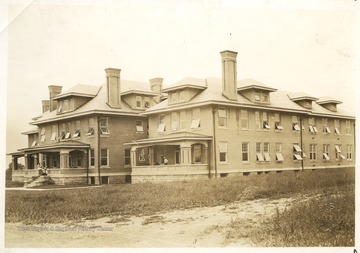 Monongalia County Hospital on the corner of Willey and Prospect Streets in Morgantown, W. Va.  Nurses appear on the porch of the left building, and two men are on the porch of the right building.