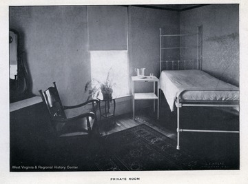 A private patient room at the New City Hospital in Morgantown, W. Va.  In addition to a metal hospital bed, the room also includes a side chair, table with plant, and dresser with mirror.