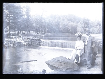 A couple poses near the dam, and others are visible on the left bank of the river.