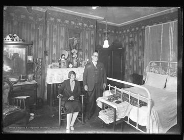 Interior bedroom of a home located in Franklin, W. Va.  A couple are the subjects of the portrait, and the photographer can be seen in the mirror's reflection.