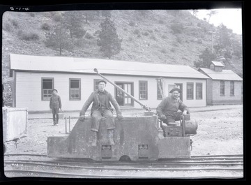 Two men sit on track mounted engine outside of mine 
