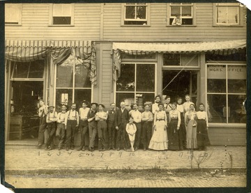 Reverse reads:"This picture shows the staff of The Morgantown Printing and Binding Company.Number 1 is Gilbert Miller.Number 8 is H. A. Cristie.Number 9 is Mr. Ludwig, General Manager.The plant is located in the rooms now occupied by Benny the Tailor and Pikes Bakery on the north side of Pleasant Street, between High and Spruce."