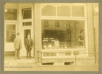 Two men stand outside the entrance to Barbe and Davis Hardware and the office of Dr. G. M. Joseph, Physician and Surgeon on Walnut Street. 