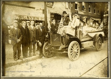 A group of men pose by a car decorated as a parade float. Note the WVU banner. 