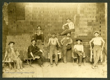 A group of brick workers pose in front of a pile of bricks.