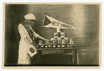Young woman pictured with display of 4-H Club items, holding flag that reads "Demonstration Girls Club."
