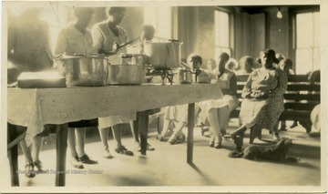 Two women show the others a scheme for removing jars from a canning boiler.