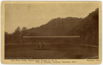 Two men pose in a boat in front of a covered bridge on the Cheat River.