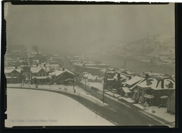 Photo features snow covered Morgantown, with the Westover Bridge in background.  The intersection of University Avenue and Willey Street is at the foreground.