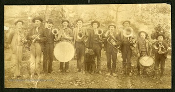 A brass ensemble from Webster Springs, made up of men and boys, poses in the woods with a dog.