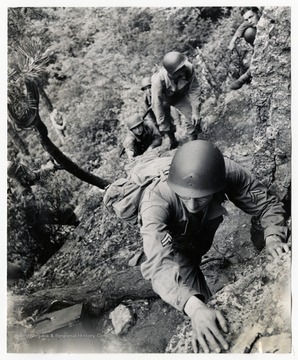A group of soldiers are trained in mountain climbing at Seneca Rocks during WWII.The back of the photo reads:"Some of Uncle Sam's soldiers will be able to vie with the best of the Swiss mountain climbers. A new phase of strenuous ground training for combat units really gives our fighting men something to sweat about. High up in West Virginia's mountains, men of the U.S. Army get a short tough course on how to overcome obstacles no matter how high. When the men complete the short period of training they're tops in their field. Under the best tutors and instructors in the art of scaling walls of sheer rock, they learn all there is to know about cliffs and mountains- except yodeling.PHOTO SHOWS: The going gets tougher and tougher the higher they get. Here a group of soldiers leave the thicket to begin the hard climb over sheer rock to reach the peak of Seneca Rock."