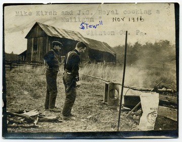 Two members of the Army Corps of Engineers cook over a fire.