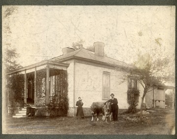 Anthony Bowen and Cora Kelley stand in front of a house with several cows. Cora has two birds on her shoulder and arm.