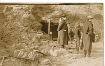 Men in coats stand outside a mine entrance.