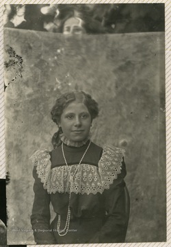 Portrait of Georgia Emma Gibson (1886-1911). A man's head is peeking over the photograph backdrop. 